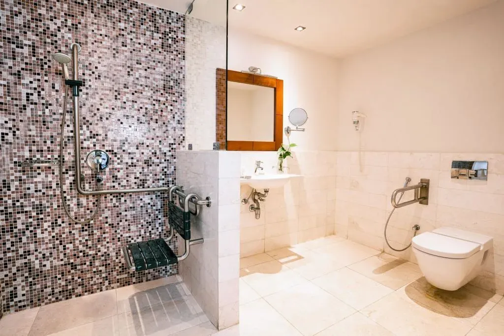 Accessible bathroom with mosaic tiled shower, grab bars, sink, and modern toilet in a spacious layout.
