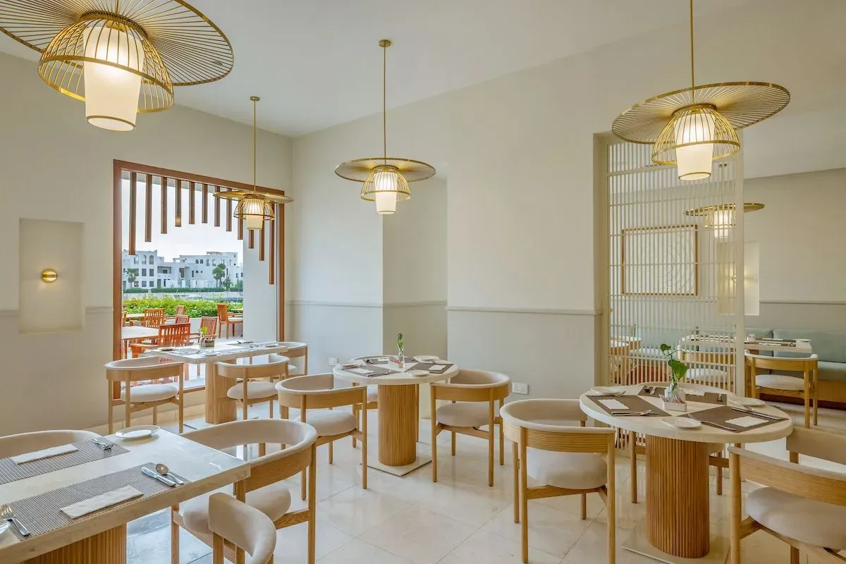 Elegant restaurant interior with circular tables, light wooden accents, and large windows overlooking a view.