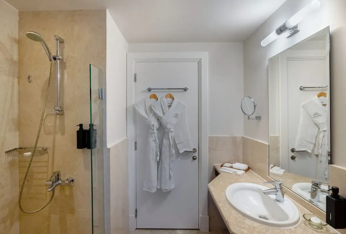 Modern bathroom featuring a glass shower, sink, and plush robes hanging on the door.