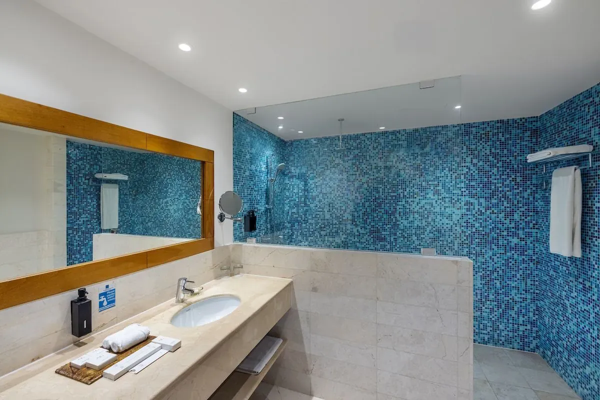 Modern bathroom with blue mosaic tiles, large mirror, sink, and shower area with minimalist design.