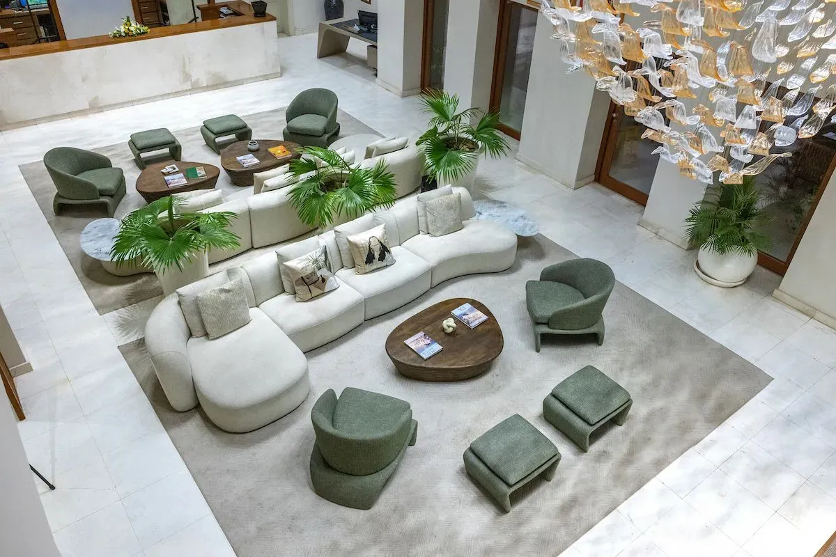 Luxurious hotel lobby featuring modern sofas, green chairs, and decorative plants, illuminated by an ornate chandelier.