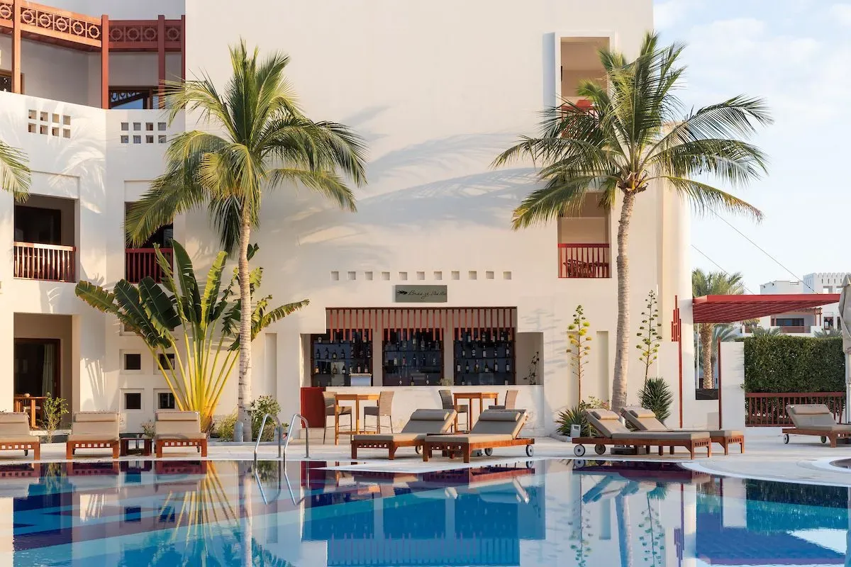 Elegant Breez Bar at Sifawy Boutique Hotel in Jebel Sifah, Oman, with palm trees and loungers by the pool.