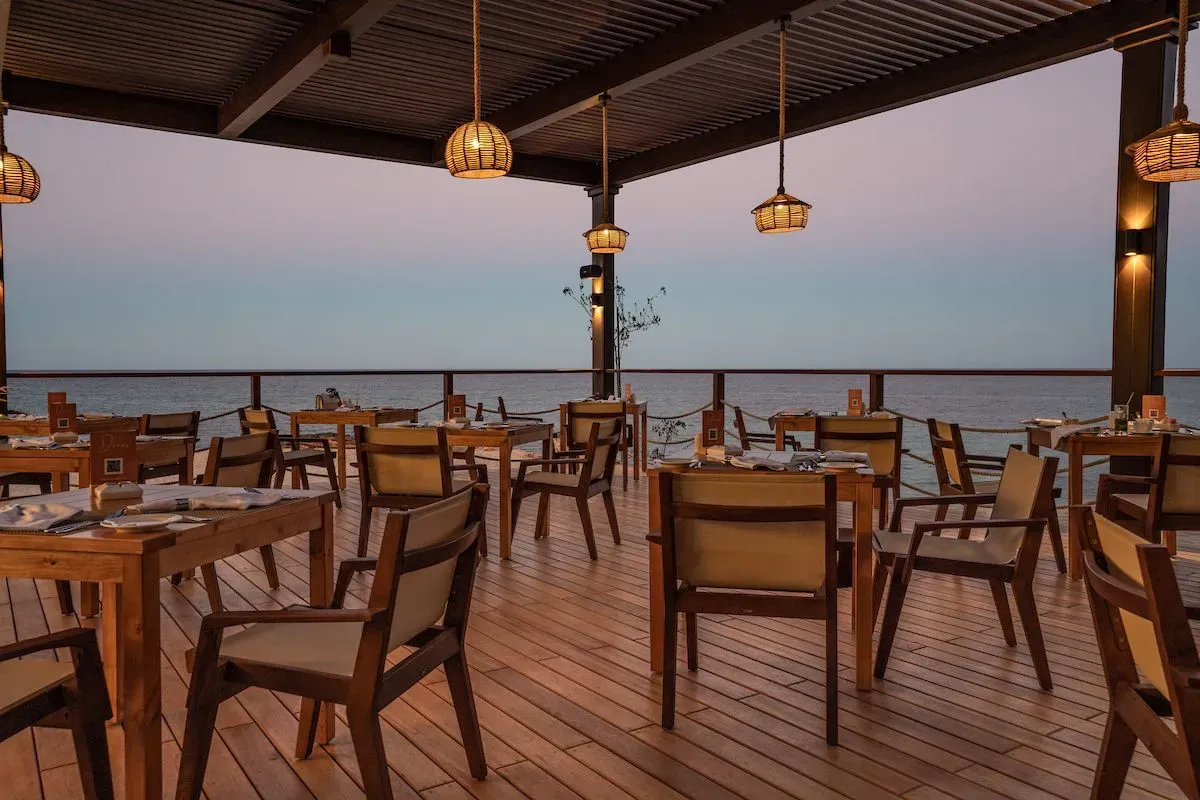 Outdoor dining area at Sifawy Boutique Hotel, featuring wooden tables and chairs with a view of the sea at sunset.