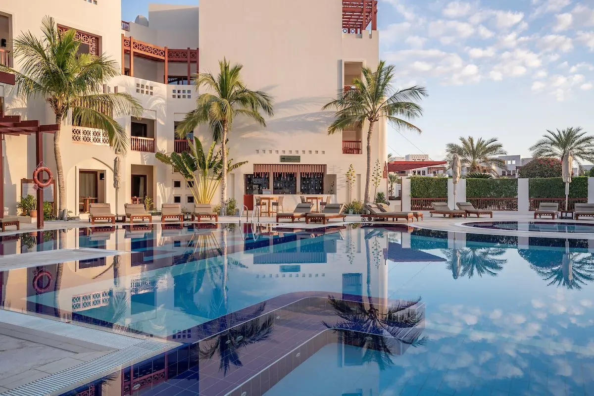 Serene view of Sifawy Boutique Hotel pool in Jebel Sifah, Oman, featuring palm trees and reflection in clear water.
