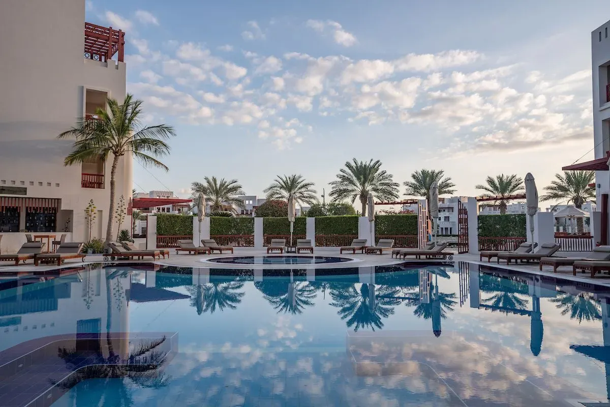 Reflective pool surrounded by lounge chairs and palm trees at Sifawy Boutique Hotel, Jebel Sifah, Oman.